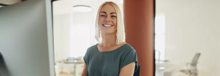 Pessoa sorrindo em frente a um computador em um escritório.