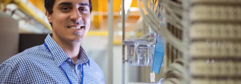 Homem sorrindo em sala de servidores com cabos ao fundo.