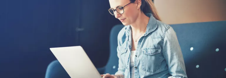 Mulher de óculos usando laptop no sofá.