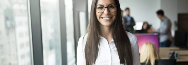 Mulher sorrindo em um escritório moderno com colegas ao fundo.