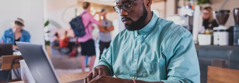 Homem com camisa verde trabalha em um laptop em um café.