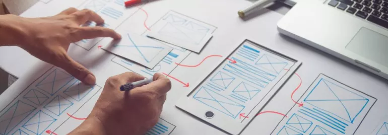 Pessoa criando design de interface em papel com laptop.