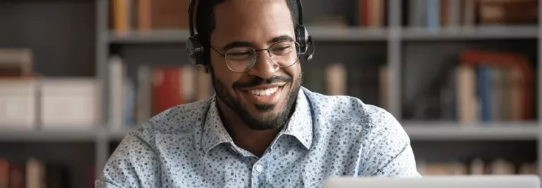 Homem sorrindo usando fones de ouvido, olhando para o laptop.