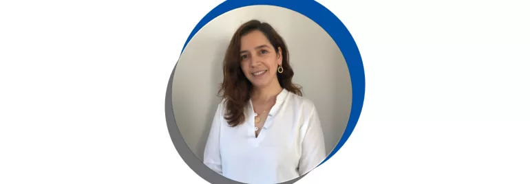 Mulher sorrindo de camisa branca em fundo azul e cinza.