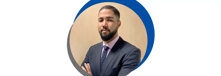 Homem de barba em terno escuro, braços cruzados.