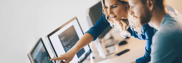 Duas pessoas trabalhando em computadores, colaborando em projeto.