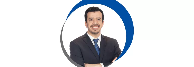 Homem sorridente em terno, fundo branco, circulo azul e cinza.