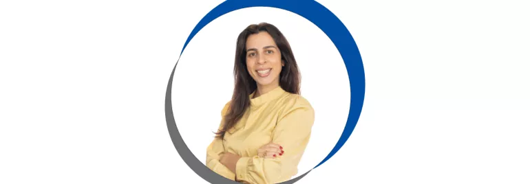 Mulher sorridente com blusa amarela, braços cruzados.