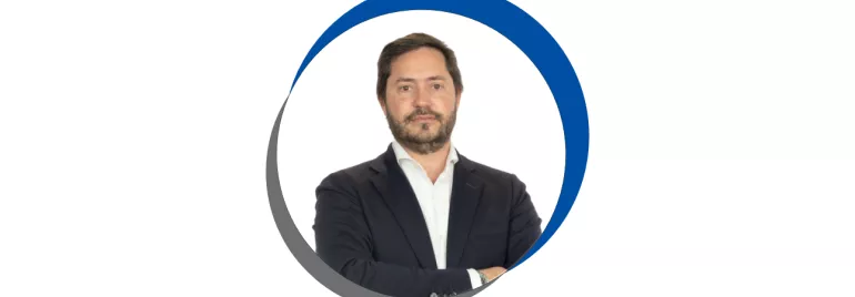 Homem de terno e barba, em fundo branco com círculo azul.