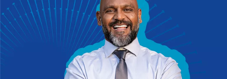 Homem sorrindo em fundo azul, vestindo camisa social.