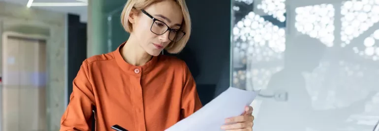 Mulher loira com óculos a ler uma folha de papel 