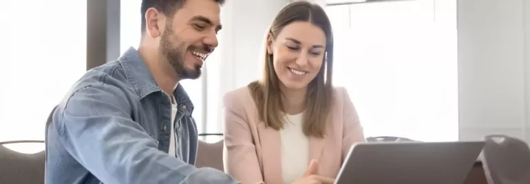 Duas pessoas sentadas à mesa, em frente a um computador portátil, a sorrir durante um momento de integração profissional.