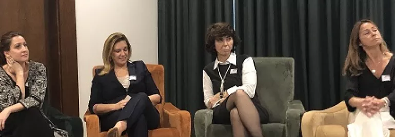 Quatro mulheres sentadas em cadeiras coloridas durante um evento.
