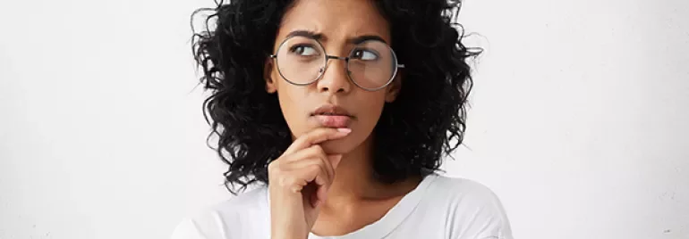 Mulher de óculos pensando, mão no queixo.