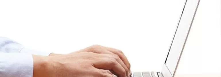 Mãos digitando em um laptop sobre uma mesa.