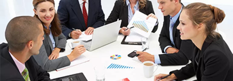 Grupo de pessoas em uma reunião com gráficos e laptops.