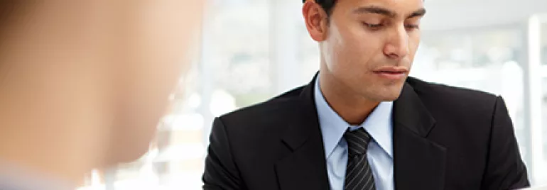 Homem de terno examinando documento em reunião.