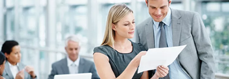 Dois colegas de trabalho analisando um documento na sala de reunião.