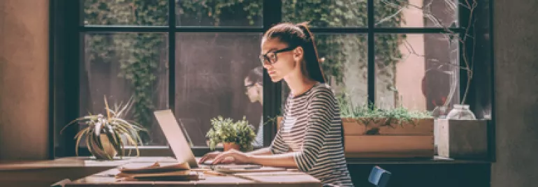 Mulher trabalhando em laptop em um café iluminado pelo sol.