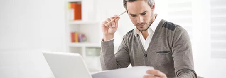 Homem analisando documentos em frente ao laptop.