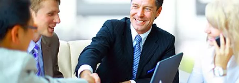 Grupo de pessoas em reunião de negócios, com homem sorrindo e apertando mãos.
