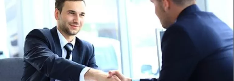 Dois homens de terno se cumprimentando em um escritório moderno.