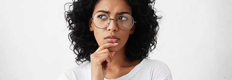 Mulher com cabelo cacheado e óculos, expressão pensativa.