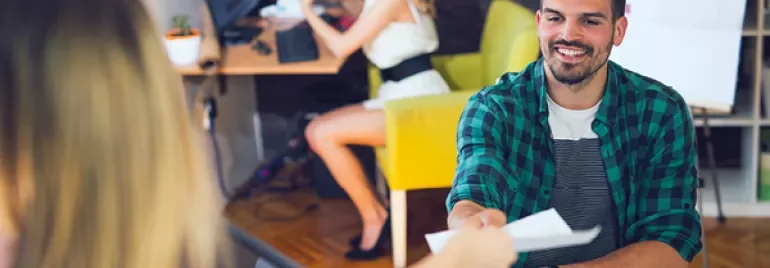 Homem sorridente recebendo documento em escritório moderno.