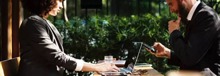 Duas pessoas em uma reunião ao ar livre com laptops e celulares.