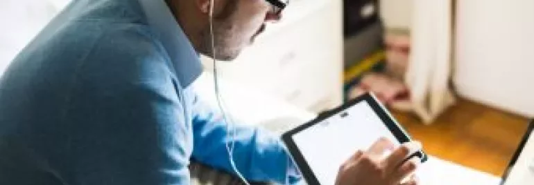 Homem usando fones de ouvido e olhando para um tablet.