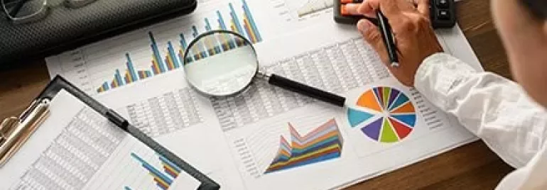 Pessoa analisando gráficos e fazendo cálculos com uma calculadora.