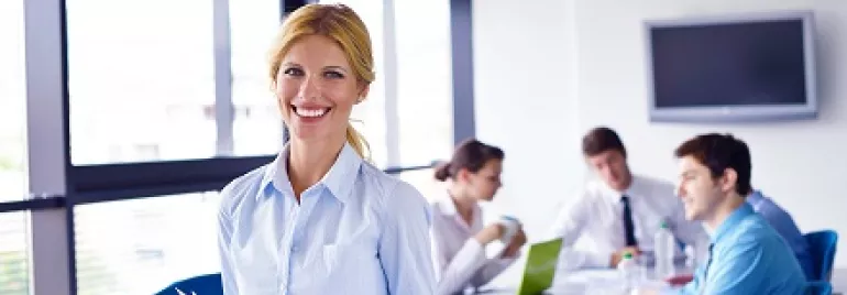 Mulher sorrindo com papéis na mão em sala de reunião.