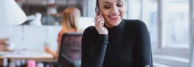 Mulher sorrindo ao telefone em um escritório moderno.
