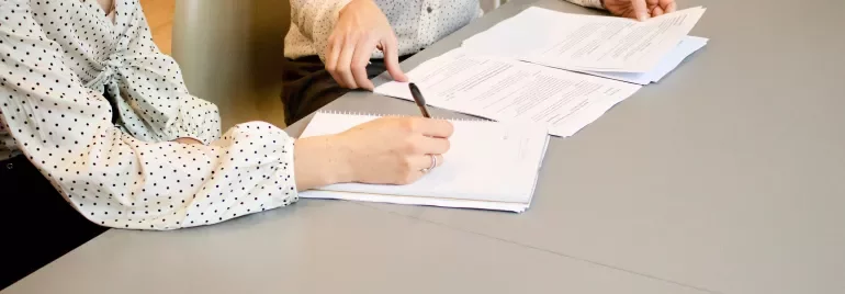 Duas pessoas revisando documentos na mesa.