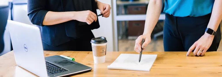 Duas pessoas discutem em frente a um laptop em uma mesa de escritório.