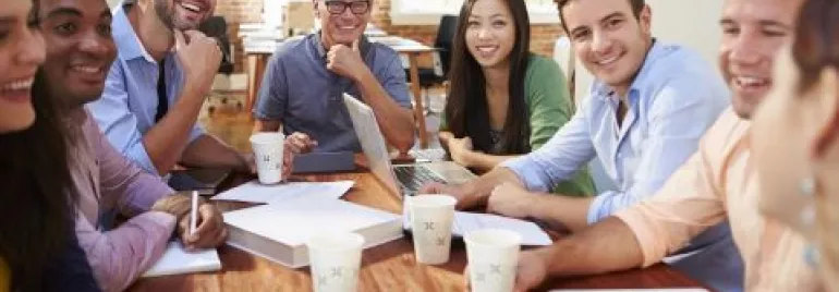 Grupo de pessoas sorrindo em uma reunião ao redor de uma mesa.