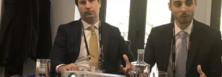 Dois homens de terno em reunião com projetor sobre a mesa.