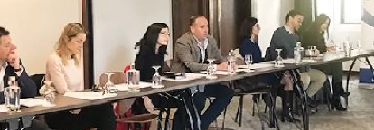 Pessoas em uma reunião sentadas em uma mesa comprida em uma sala.