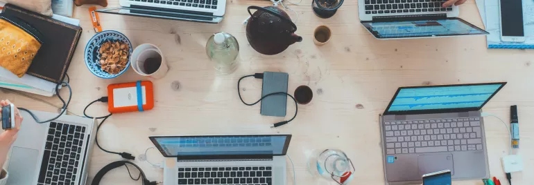 Mesa de trabalho com laptops, cadernos e xícara de café.