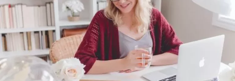 Mulher sorrindo em frente a um laptop em casa com flores na mesa.
