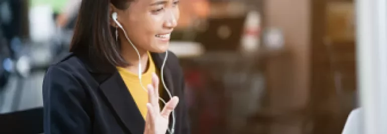 Mulher sorrindo e participando de reunião online com fones de ouvido.