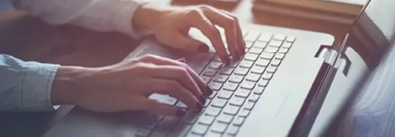 Pessoa digitando em laptop em mesa de madeira.