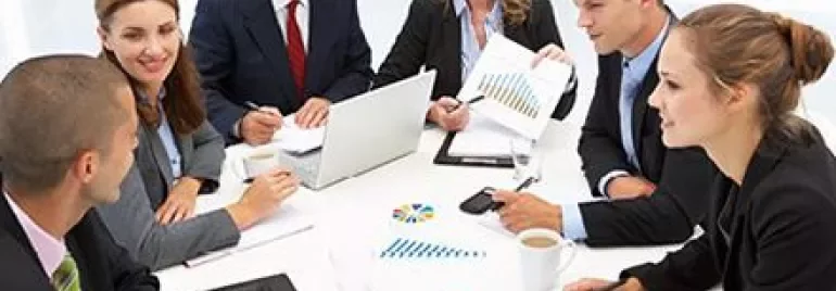 Reunião de negócios com pessoas ao redor de uma mesa, gráficos e laptop.