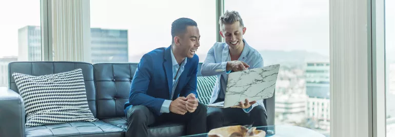 Dois homens sorrindo enquanto olham um laptop em um escritório moderno.