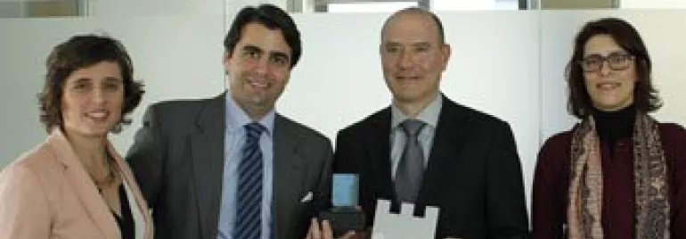 Quatro pessoas sorrindo, duas segurando troféus em um escritório.