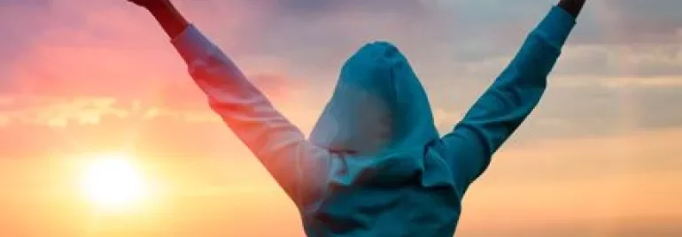 Pessoa comemorando ao pôr do sol com braços erguidos.