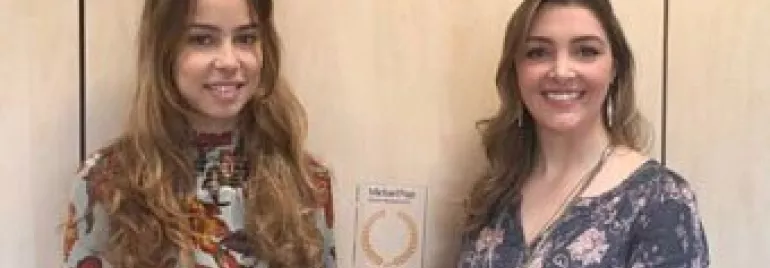 Duas mulheres segurando um prêmio. Ambas estão sorrindo.