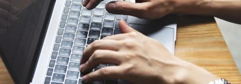 Mãos digitando em um laptop sobre uma mesa de madeira.