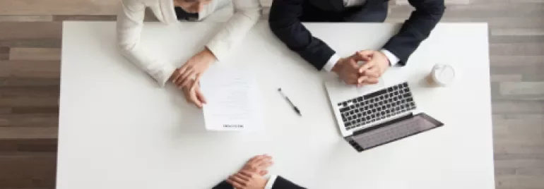 Pessoa em entrevista de emprego sentada à mesa com dois recrutadores.