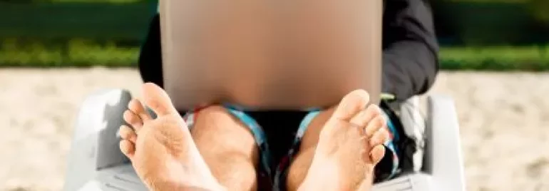 Homem de terno trabalhando em um laptop sentado na praia.